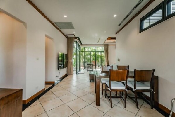 A spacious hallway with a dining area featuring wooden chairs and a television.