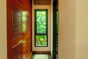 A hallway with a wooden door and a window with a view of greenery.