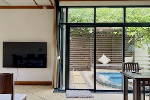 A living room with a TV, a sliding glass door leading to a patio with a pool, and a dining area. - Rose Pool Villa, The perfect private oasis (Phuket)