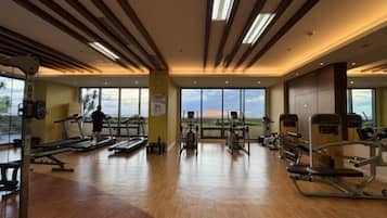 A gym with exercise equipment, large windows, and a wooden floor.