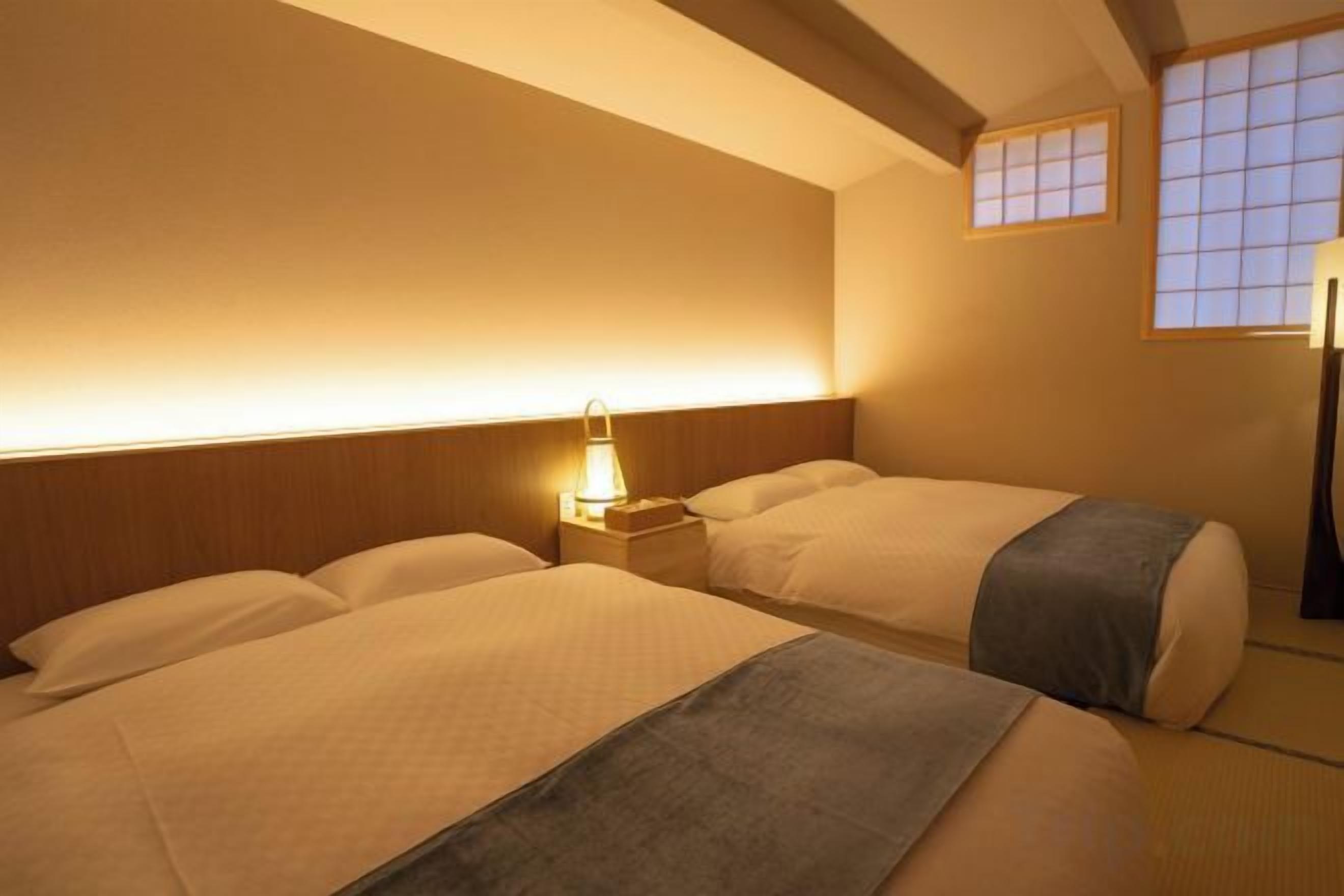 A hotel room with two beds, a bedside table with a lamp, and a window with a view.