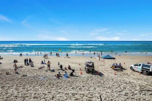 A beach with people, a lifeguard station, and a clear sky. - The Ocean Arcade - Views, Games & Vibes (Surfers Paradise)