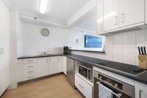 A modern kitchen with white cabinets, a built-in oven, and a microwave. - The Ocean Arcade - Views, Games & Vibes (Surfers Paradise)