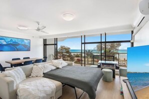 A modern bedroom with a large bed, a desk, and a view of the beach. - The Ocean Arcade - Views, Games & Vibes (Surfers Paradise)