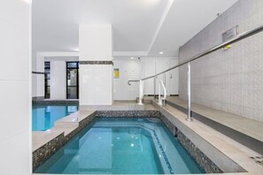 An indoor swimming pool with a tiled edge, a metal handrail, and a tiled wall in the background. - The Ocean Arcade - Views, Games & Vibes (Surfers Paradise)