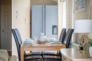 A dining area with a wooden table, black chairs, and a refrigerator in the background.