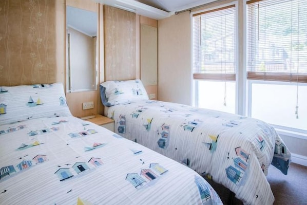 A bedroom with two beds, a window with blinds, and a mirror.