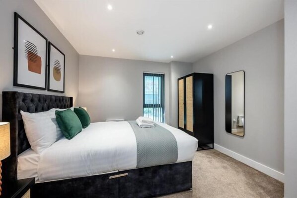A modern bedroom with a large bed, a dark headboard, and a window with blinds.