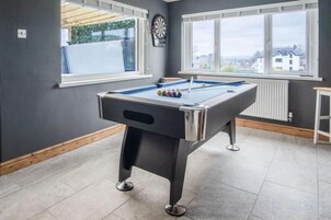 Una mesa de billar en una habitación con ventanas amplias y un dardo colgado en la pared.
