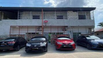 Un edificio con entrada protegida por una reja, tres coches estacionados y cielo despejado.