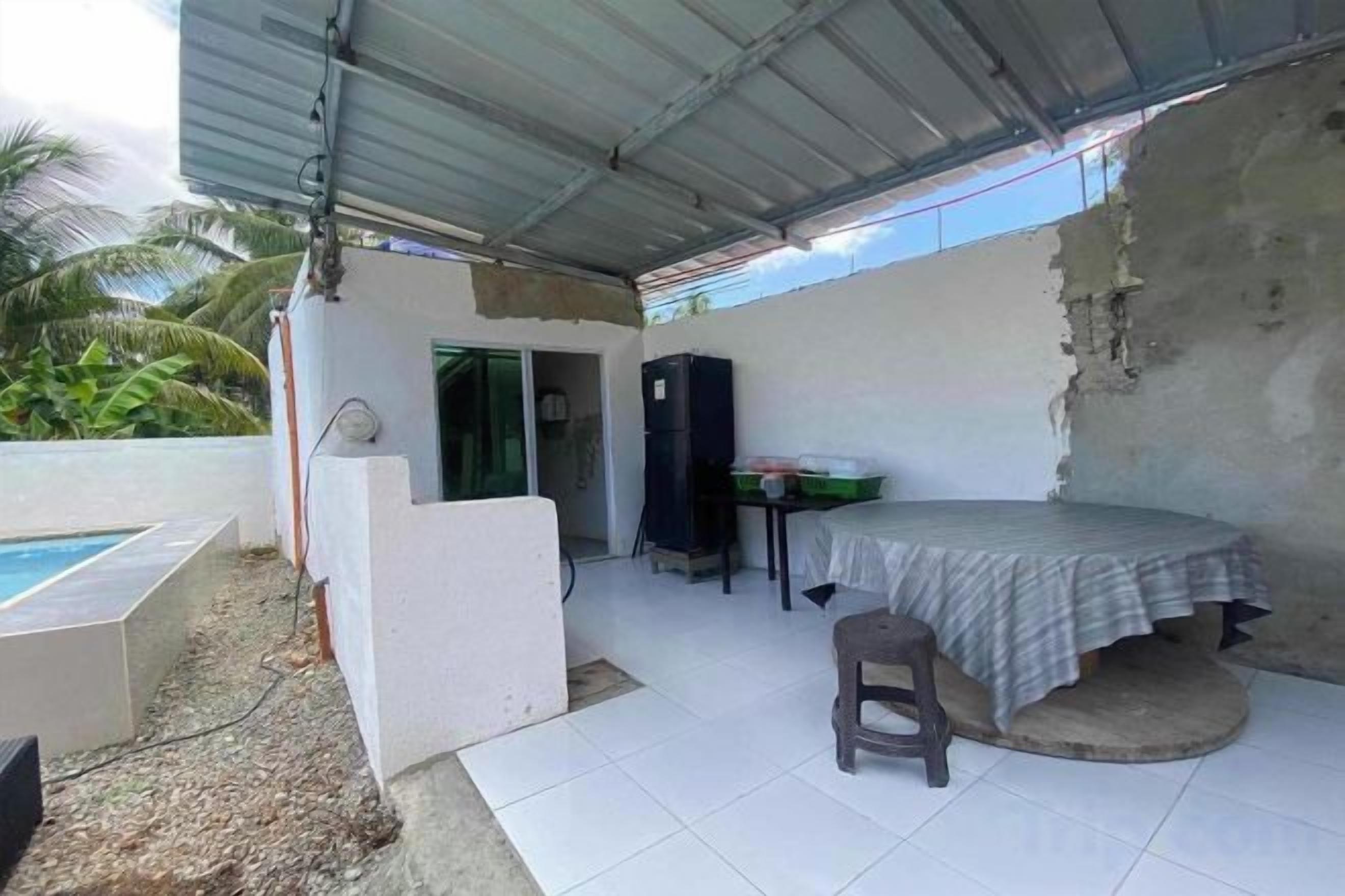 Un espacio exterior cubierto con piscina, una mesa con una silla y una pequeña cocina.