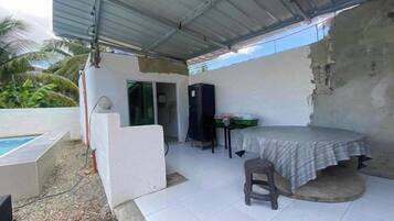 Un espacio exterior cubierto con piscina, una mesa con una silla y una pequeña cocina.