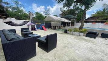 Un patio exterior con mobiliario de mimbre negro, una zona de juegos para niños y una piscina.
