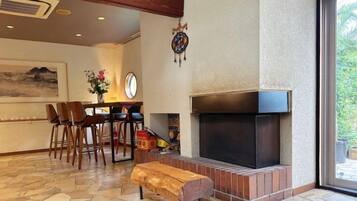 A room with a fireplace, a dining area with chairs, and a bench.