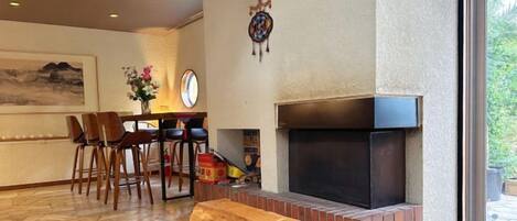 A room with a fireplace, a dining area with chairs, and a bench.