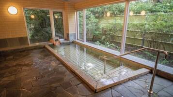 A stone-floored indoor pool with a glass barrier and a view of a garden.