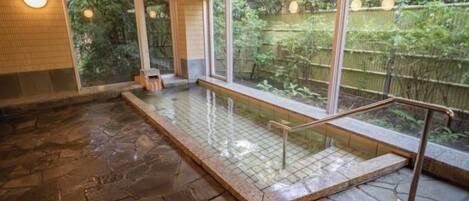 A stone-floored indoor pool with a glass barrier and a view of a garden.
