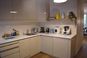 A modern kitchen with white cabinets, a countertop, and various appliances including a coffee maker, kettle, and toaster. - Splendid one bedroom in Le Marais area (Paris)