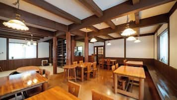 Interior de restaurante con mesas y sillas de madera, techos altos con vigas a la vista e iluminación colgante.