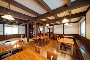 Interior de restaurante con mesas y sillas de madera, techos altos con vigas a la vista e iluminación colgante.