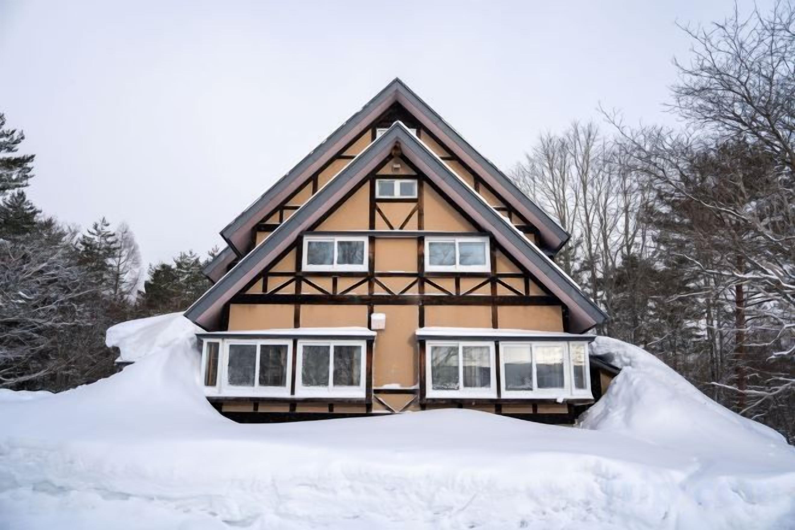 A two-story chalet with a steeply pitched roof, multiple windows, and a snow-covered ground.