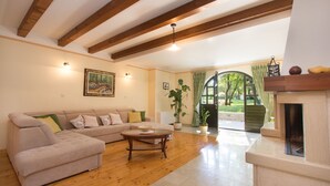 Uma sala de estar com sofá, mesa de centro e lareira. Há uma porta que dá para um jardim.