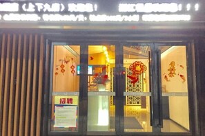 A hotel entrance with a glass door, a signboard, and a decorative red ornament.