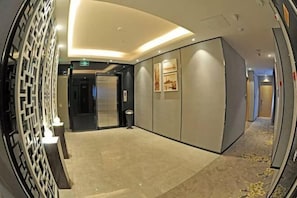 A hotel corridor with a modern design, including a wall-mounted decorative panel, a carpeted floor, and a door leading to an elevator.