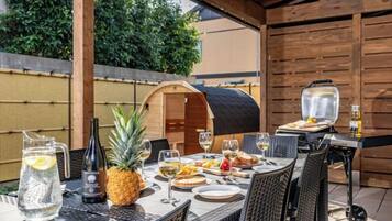 Een terras met een barbecue, rieten stoelen en een tafel gedekt met borden, glazen en een ananas.