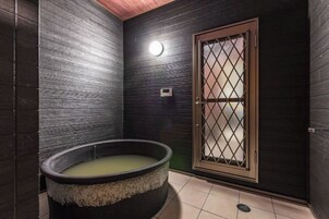 Una habitación con una bañera, una puerta con diseño de cuadrícula y una lámpara en la pared.