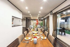 Zona de dinar amb una taula de fusta llarga preparada per a un àpat, envoltada de cadires, i amb vistes a l'exterior a través de grans finestres.