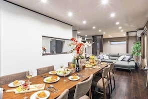 A modern dining area with a long wooden table, multiple chairs, and a variety of dishes and drinks. - PEACE OF REST TAKASHIMA (Takashima)