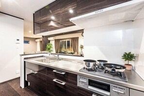 A modern kitchen with a large island, stainless steel appliances, and dark wood cabinetry. - PEACE OF REST TAKASHIMA (Takashima)