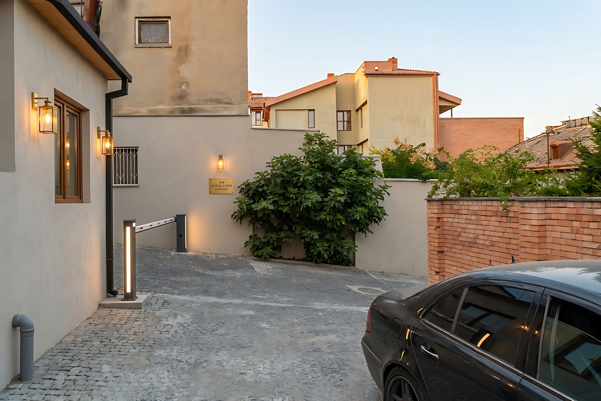 Una strada residenziale con vialetto lastricato, un'auto parcheggiata a destra e un edificio con ingresso chiuso da cancello.