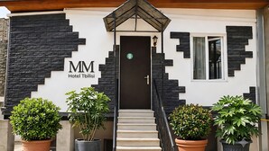 Entrada de hotel con diseño moderno, fachada de piedra, una escalera que conduce a la puerta y plantas en macetas a la entrada.