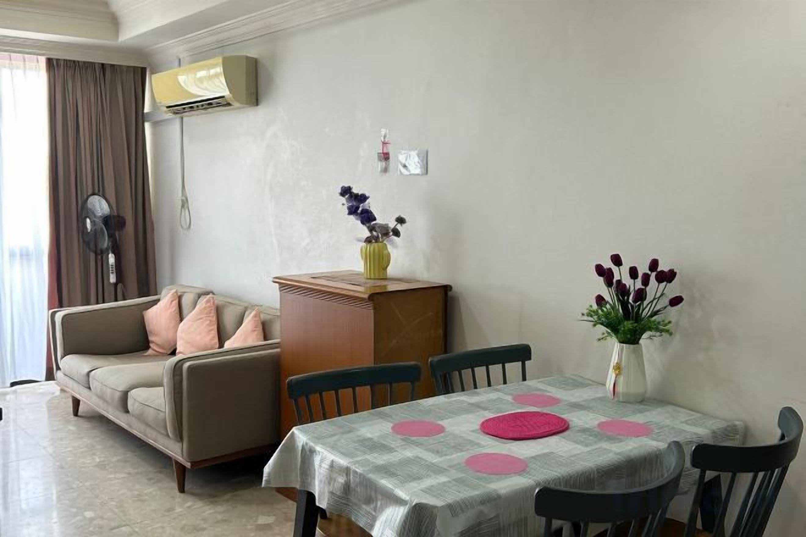 A dining area with a table set for two, a sofa, and a vase with flowers.