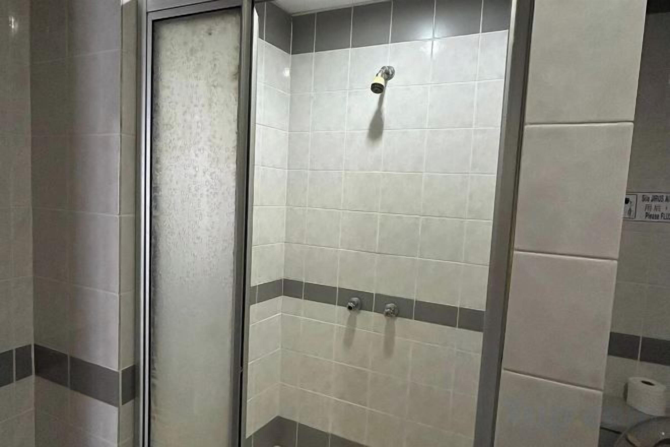 A shower with a glass door and tiled walls, a showerhead, and a towel rack.
