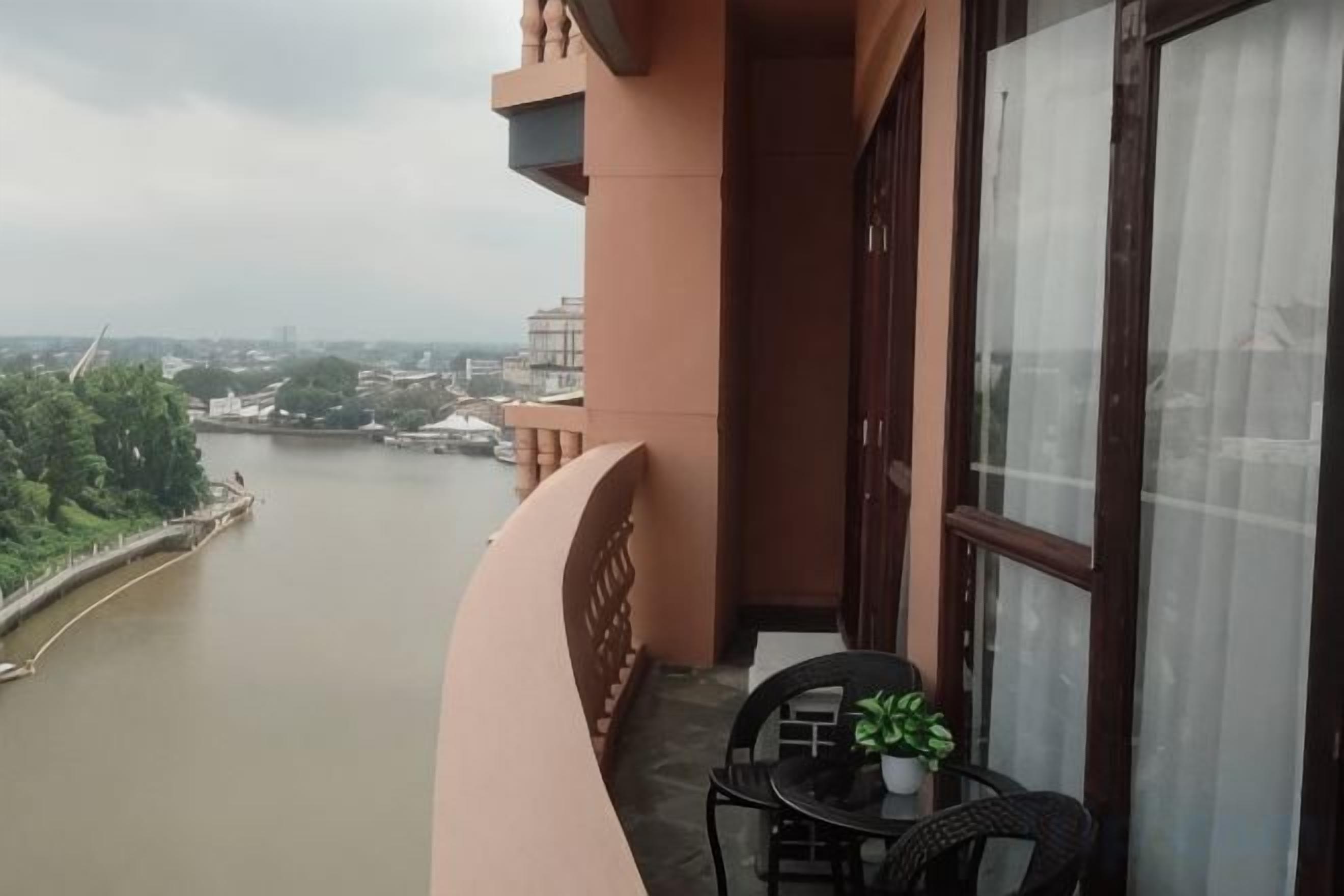 A balcony with a view of a river, a table with a potted plant, and a window with curtains.