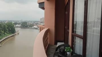 A balcony with a view of a river, a table with a potted plant, and a window with curtains.