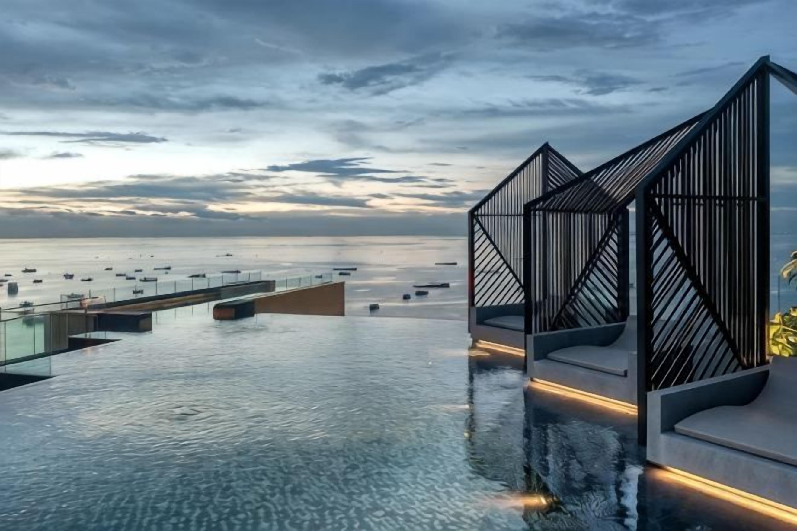 An infinity pool with a view of the sea and boats, modern architectural structures, and a clear sky.
