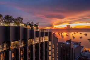 A waterfront hotel with multiple floors, balconies, and a view of the sunset over the water. - The Edge Central Pattaya - infinity pool with sea view (Pattaya)