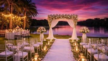 An outdoor wedding venue with a floral arch, tables, chairs, and a pathway leading to the arch.