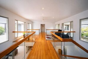 Un interior moderno con piso de madera central, barandas de vidrio y ventanas amplias.