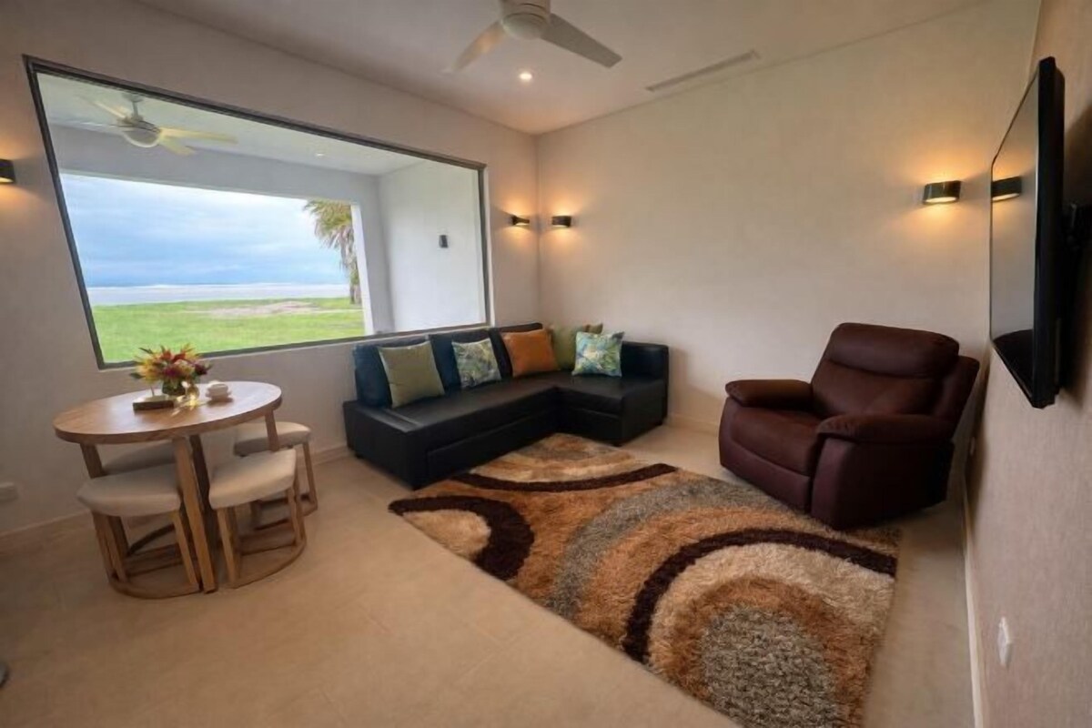 Una sala de estar moderna con un ventanal grande, un sofá, un sillón reclinable y un comedor.