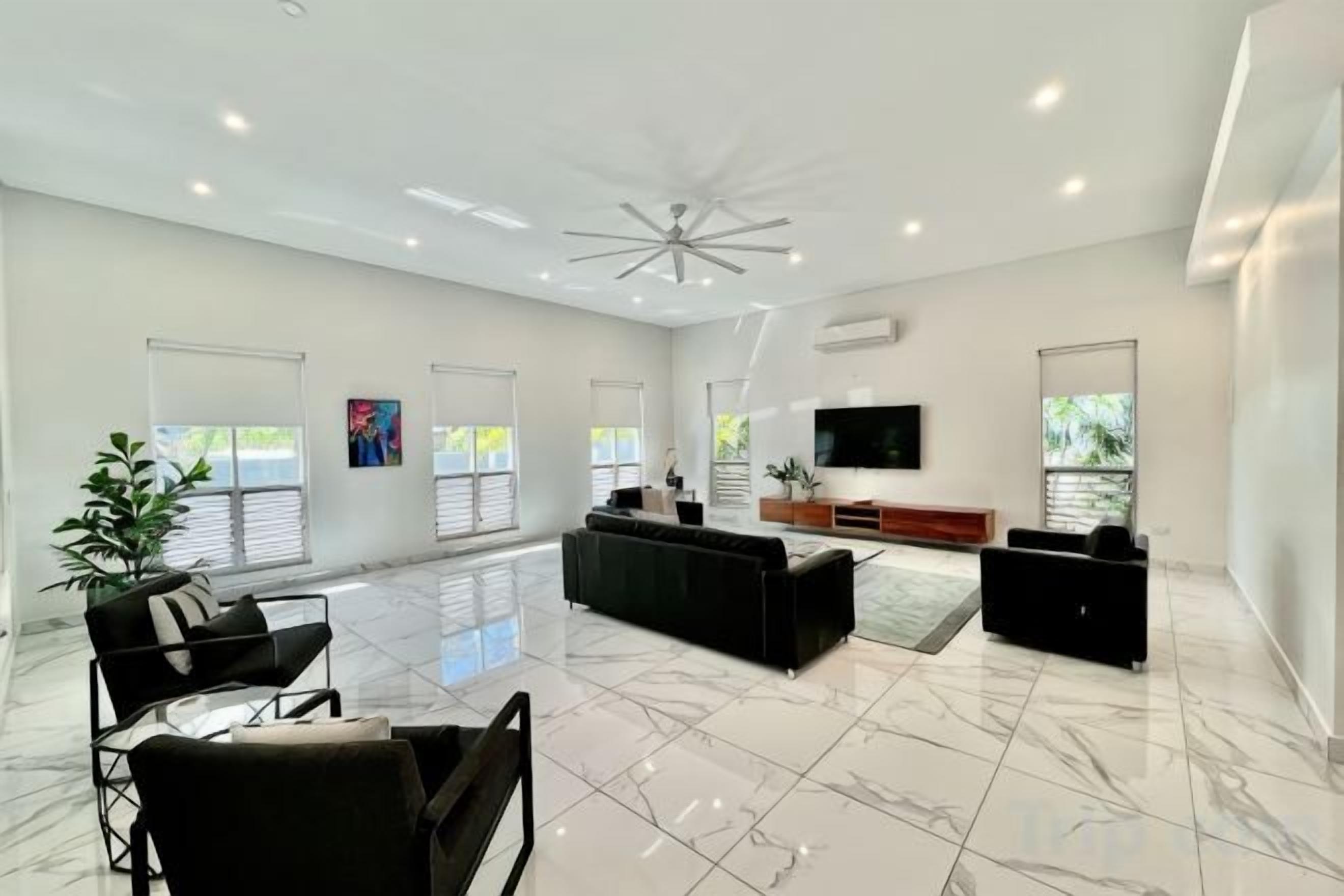 Un salón espacioso con un televisor grande, sofás negros y suelo de mármol.