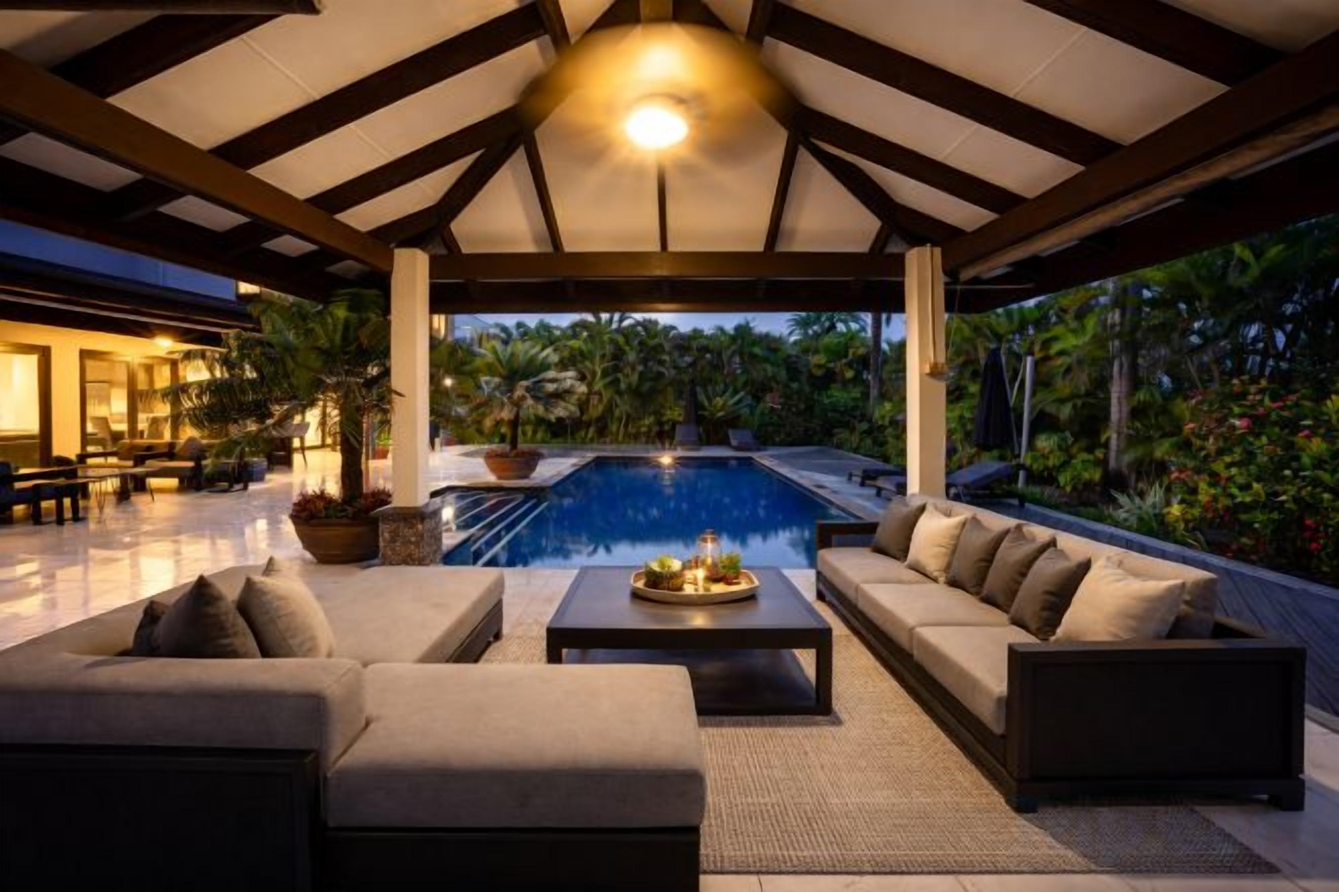 A covered outdoor area with a pool, seating, and potted plants.