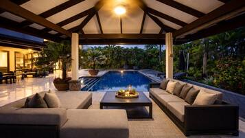 A covered outdoor area with a pool, seating, and potted plants.