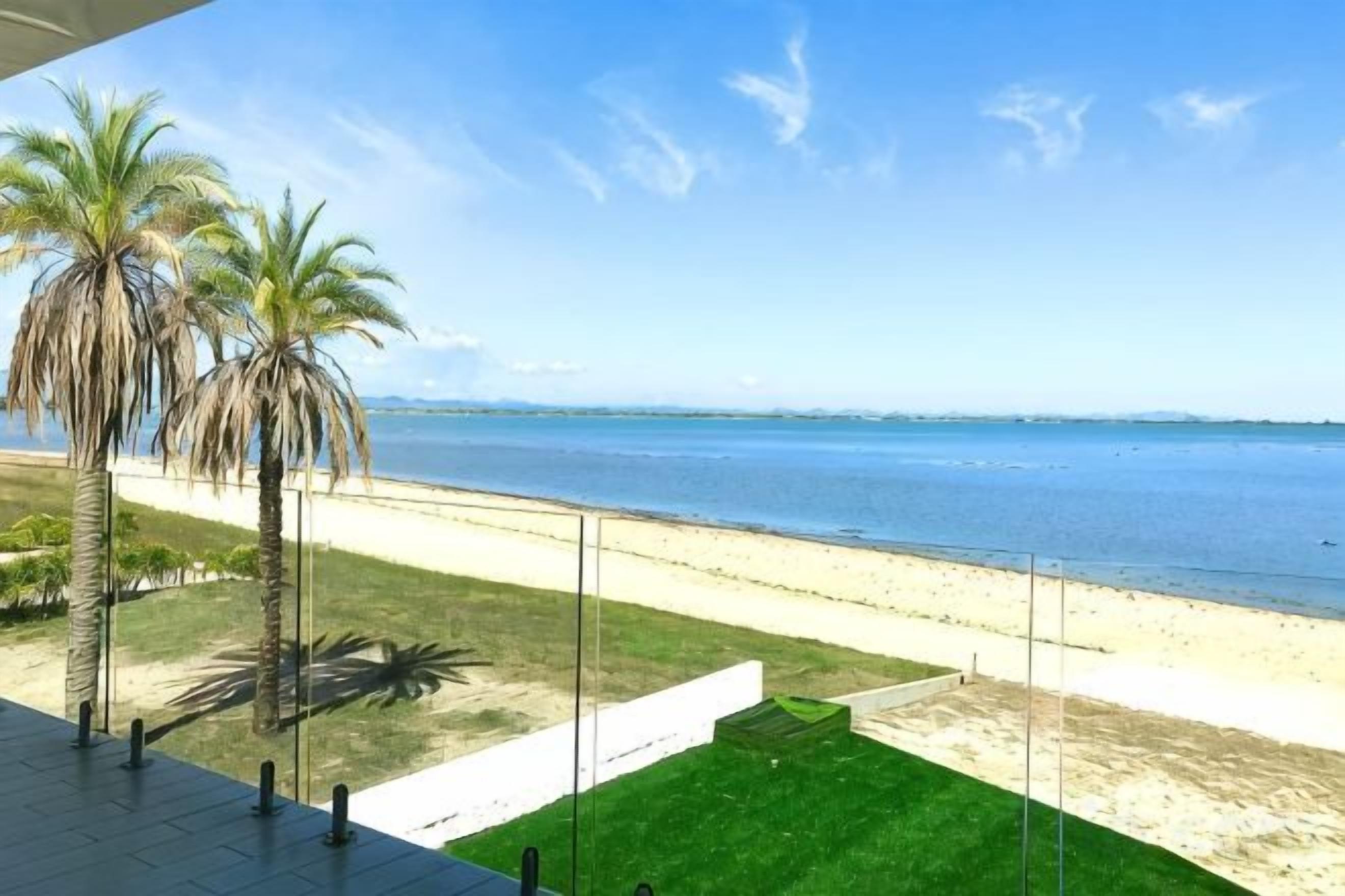 Vista a la playa desde un balcón con palmeras y cielo despejado.