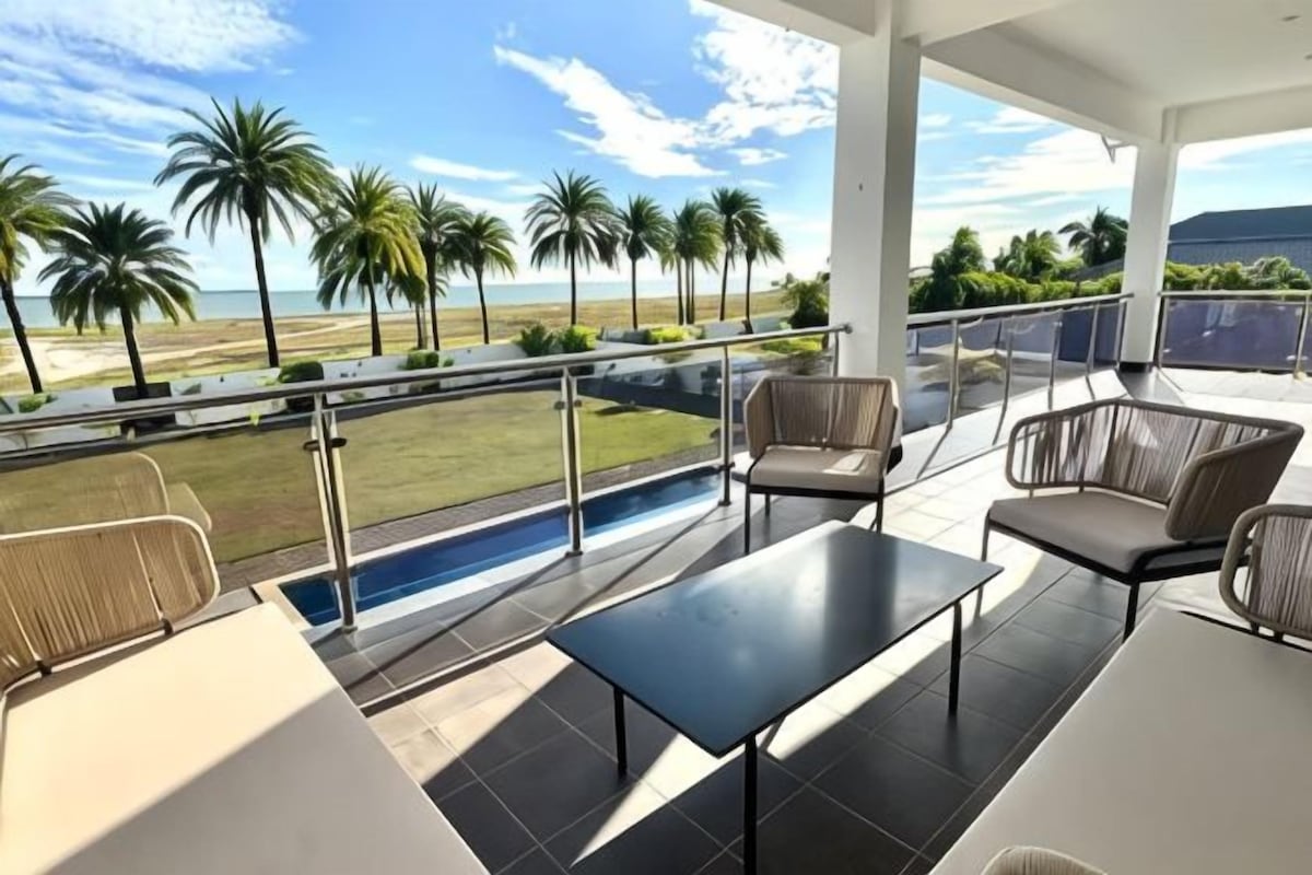 Un balcon avec une piscine, un espace salon et une vue sur l’océan et les palmiers.