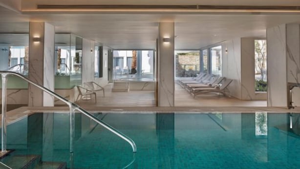 Una piscina interior con paredes de vidrio transparente, sillas de descanso y un diseño moderno.